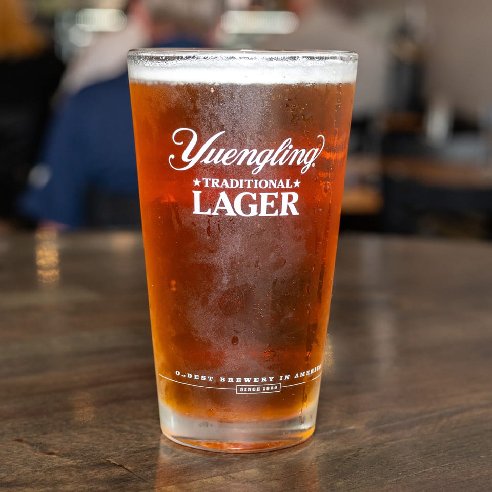 A frosty glass of Yuengling Traditional Lager with a foamy head sits on a wooden table.