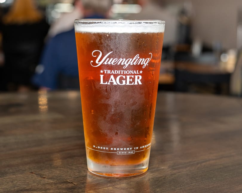 A frosty glass of Yuengling Traditional Lager with a foamy head sits on a wooden table.