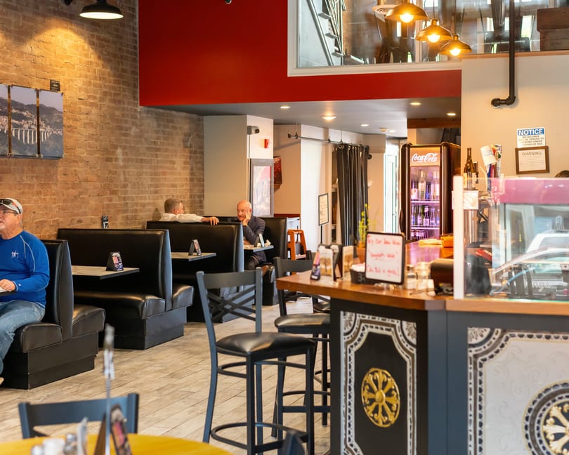 Restaurant interior with brick walls, black booths, and a counter with bar stools.