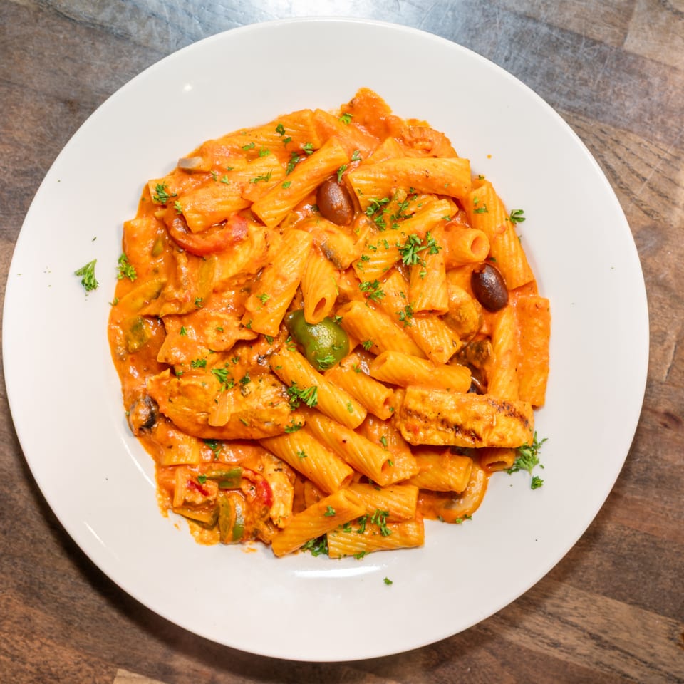 Rigatoni pasta with chicken, olives, bell peppers, and parsley in a creamy tomato sauce.