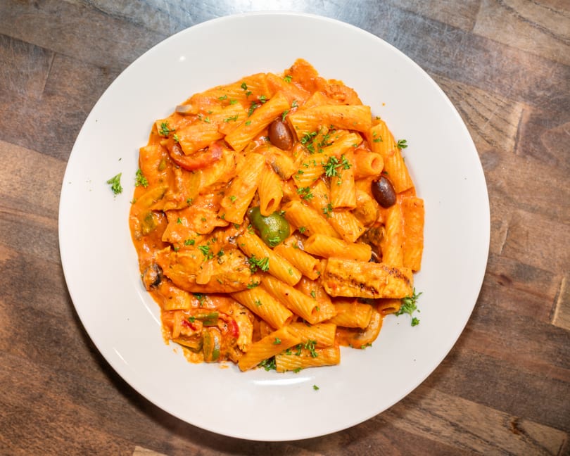 Rigatoni pasta with chicken, olives, bell peppers, and parsley in a creamy tomato sauce.