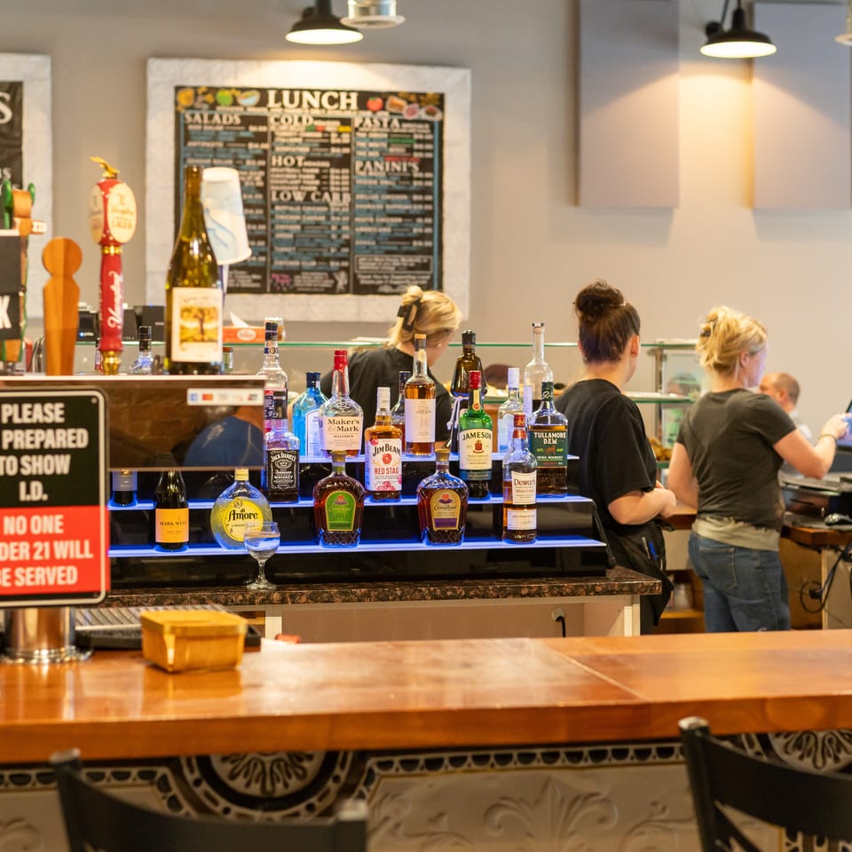 A bar with various liquor bottles on display, a "Wine O'Clock" sign, and staff working behind the counter.