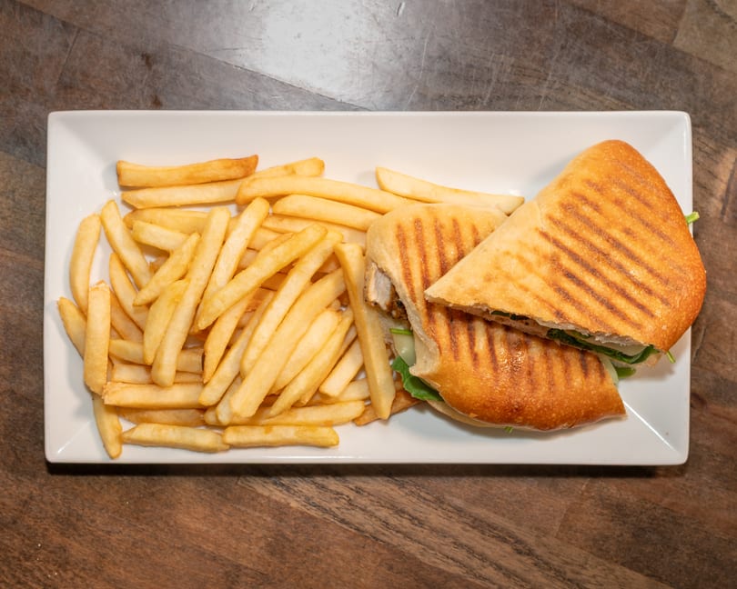 Grilled panini sandwich with chicken, cheese, and spinach, served with a side of golden french fries.