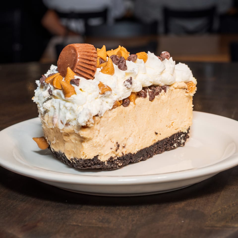 A slice of peanut butter pie with whipped cream, chocolate chips, and a peanut butter cup.