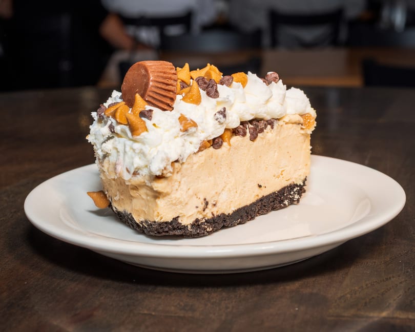 A slice of peanut butter pie with whipped cream, chocolate chips, and a peanut butter cup.