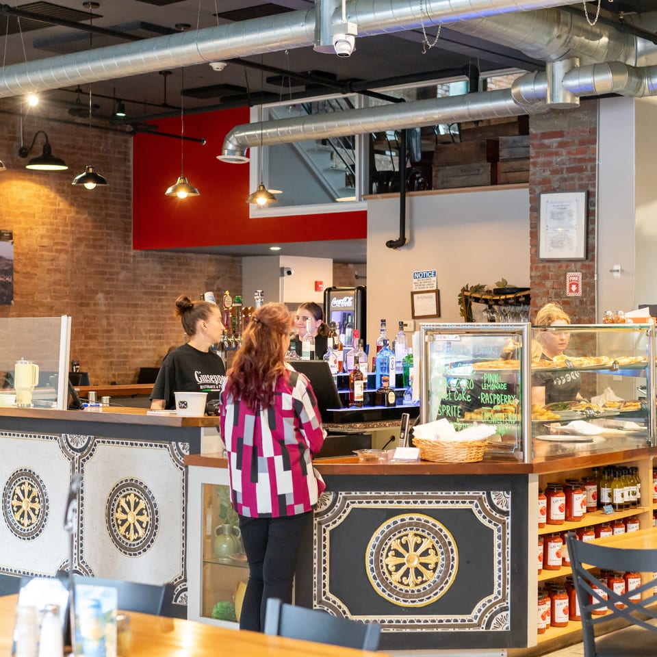 Customers ordering at a counter with a bar, display cases, and brick walls at Giuseppe's.