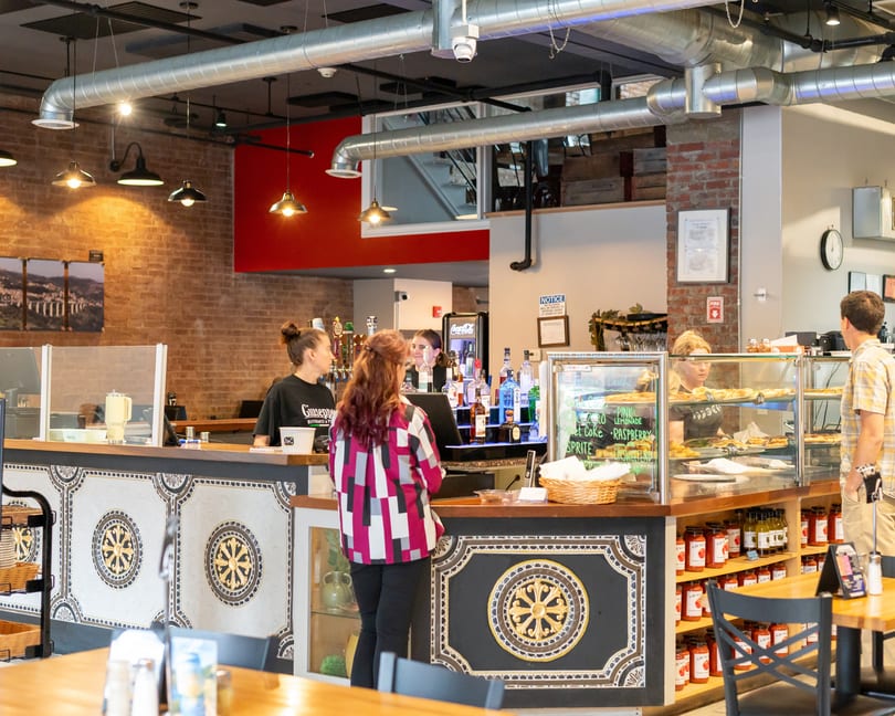 Customers ordering at a counter with a bar, display cases, and brick walls at Giuseppe's.