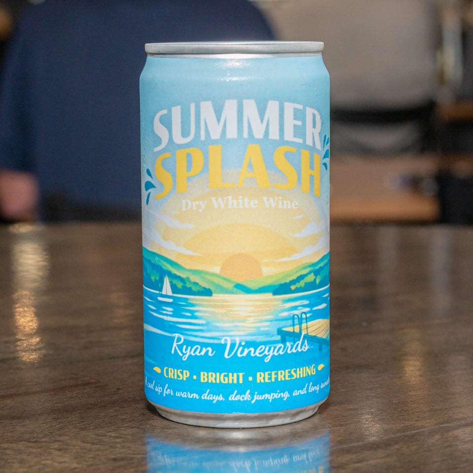 A chilled can of "Summer Splash Dry White Wine" from Ryan Vineyards, featuring a lake sunset design.