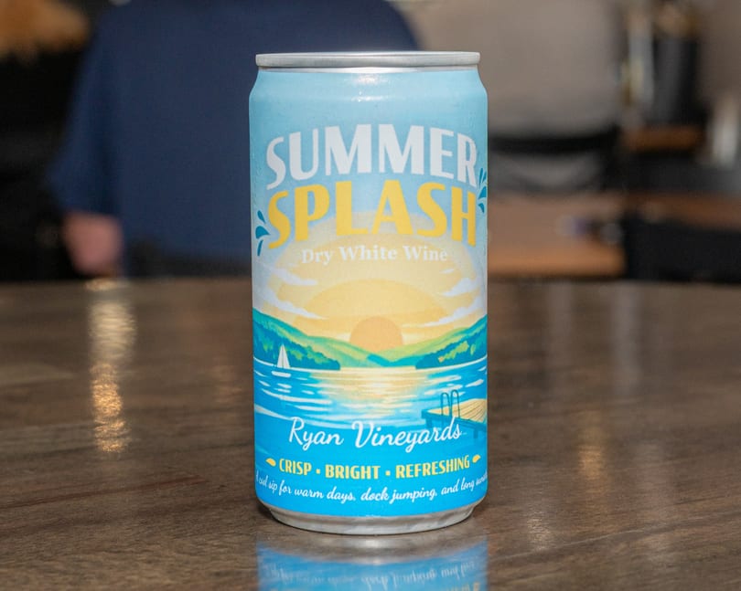 A chilled can of "Summer Splash Dry White Wine" from Ryan Vineyards, featuring a lake sunset design.