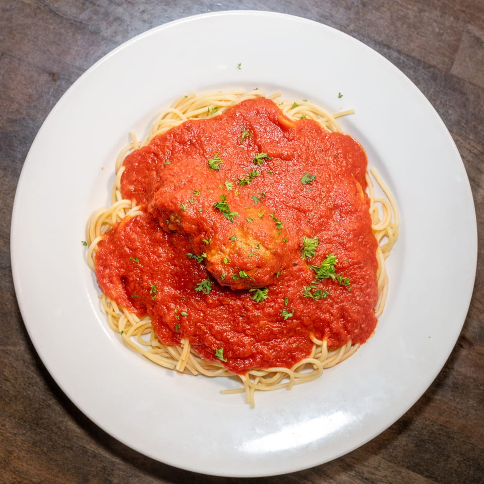 Spaghetti with a rich red marinara sauce and a large meatball, garnished with parsley.