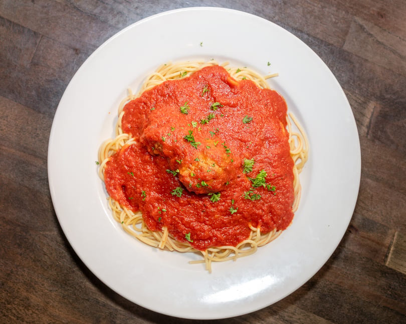 Spaghetti with a rich red marinara sauce and a large meatball, garnished with parsley.