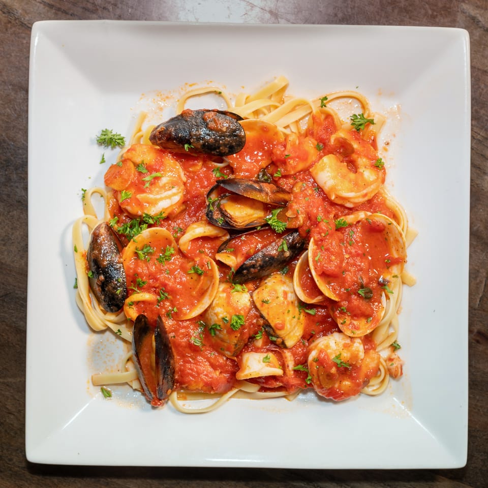 Seafood linguine with mussels, clams, and shrimp in a rich red tomato sauce, garnished with parsley.