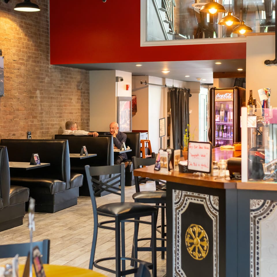 Restaurant interior with brick walls, black booths, and a counter with bar stools.
