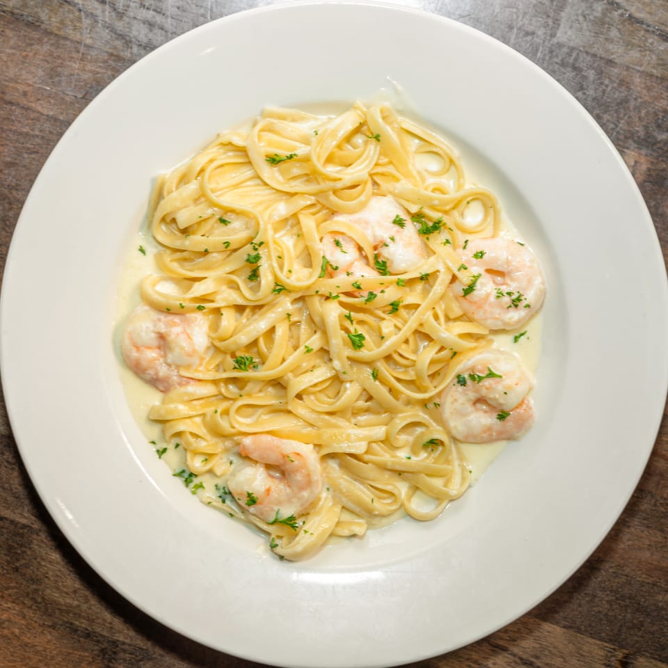 Fettuccine Alfredo with shrimp and parsley on a white plate, on a wooden table.