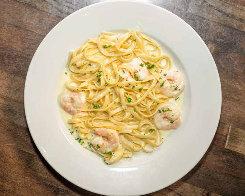 Fettuccine Alfredo with shrimp and parsley on a white plate, on a wooden table.