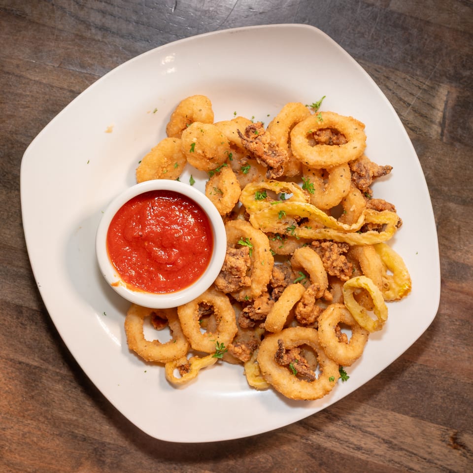 Crispy fried calamari rings and tentacles with a side of red marinara sauce on a white plate.